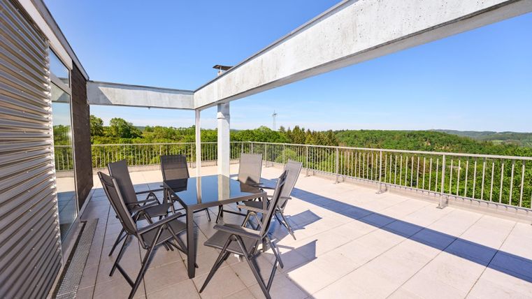 Eine moderne Teaküche mit einem Glastisch und Stühlen im Freien. Der Blick ist auf eine grüne Landschaft unter einem klaren blauen Himmel gerichtet.