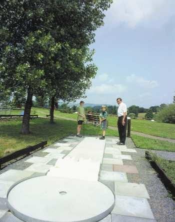 Eine Minigolfanlage mit mehreren Spielern. Im Hintergrund sind Bäume und eine grüne Wiese zu sehen.