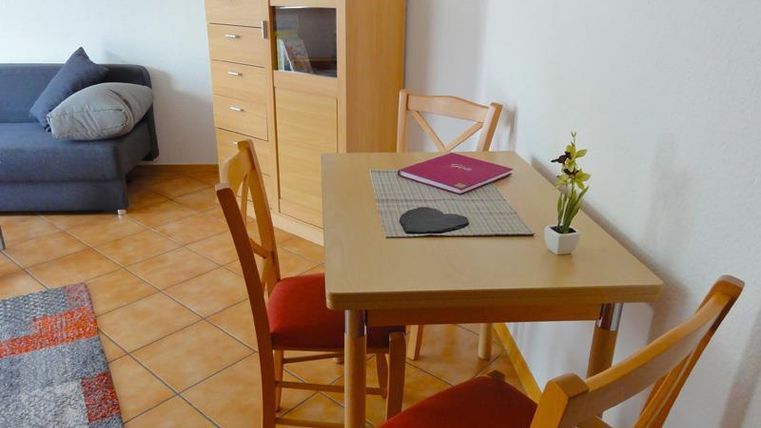 A cozy living area with a small table and chairs. In the background, there is a cupboard and a couch.
