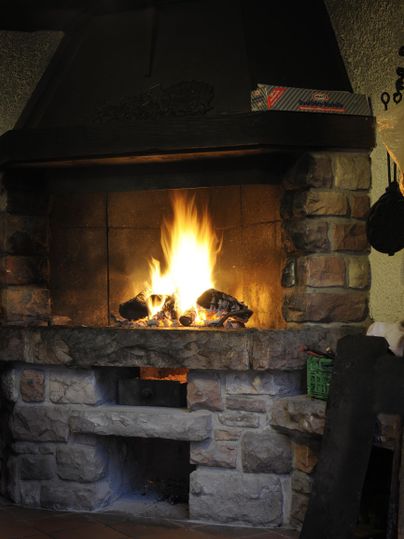 Ein gemütlicher Kamin mit flackerndem Feuer. Der Kamin ist aus Stein und vermittelt eine warme Atmosphäre.