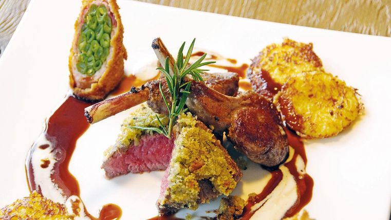 Een kunstzinnig gerecht met lamskoteletten, omringd door knapperige bijgerechten en een saus. Het eten is decoratief gepresenteerd en toont verse kruiden.