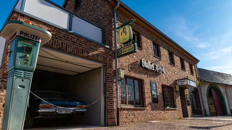 A charming building with a garage that houses a classic car. A historic gas pump completes the scene.