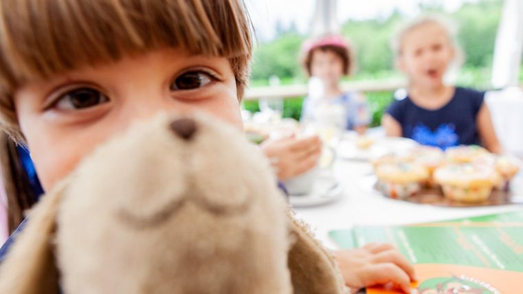 Child, with a stuffed animal, looking closely at the camera