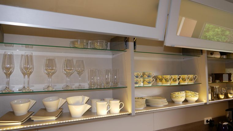 A modern kitchen display with various glasses and dishes. At the top are elegant wine glasses, and below are arranged colorful cups and plates.