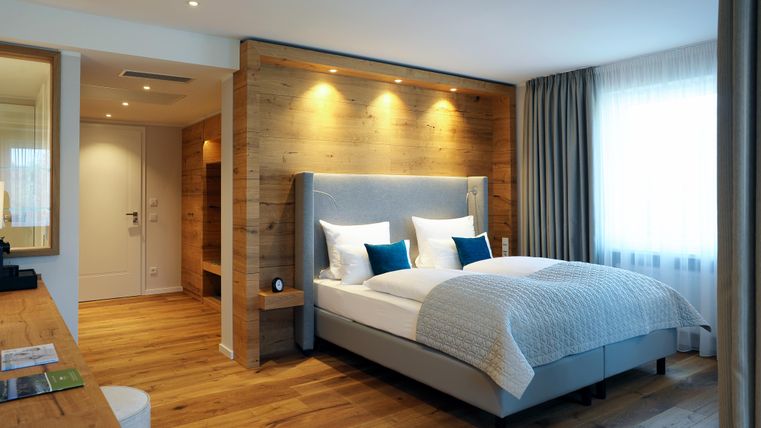 Ein modernes Schlafzimmer mit Holzwänden und einem Doppelbett. Große Fenster bieten viel Tageslicht und der Raum ist geschmackvoll eingerichtet.