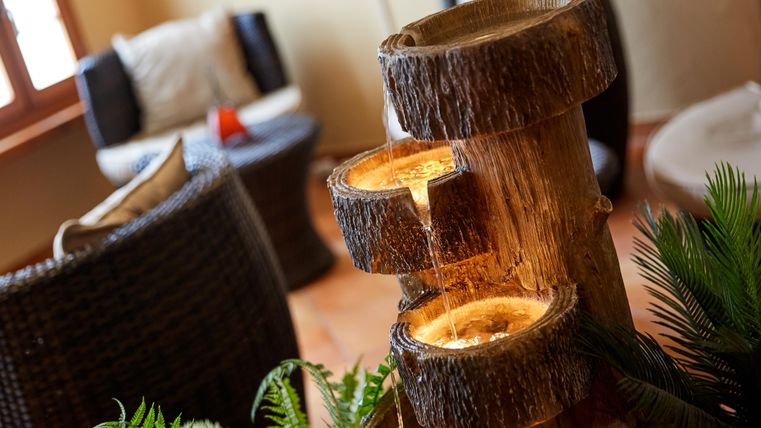 Wooden fountain with flowing water in a cozy room with rattan furniture and plants.
