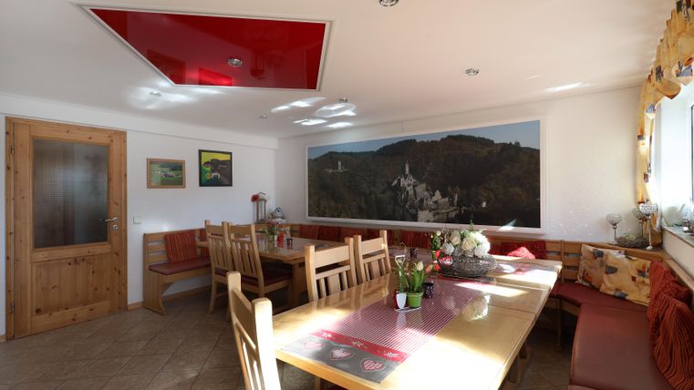 A bright dining area with a large table and benches. Pictures hang on the walls and there is a beautiful view of the landscape.