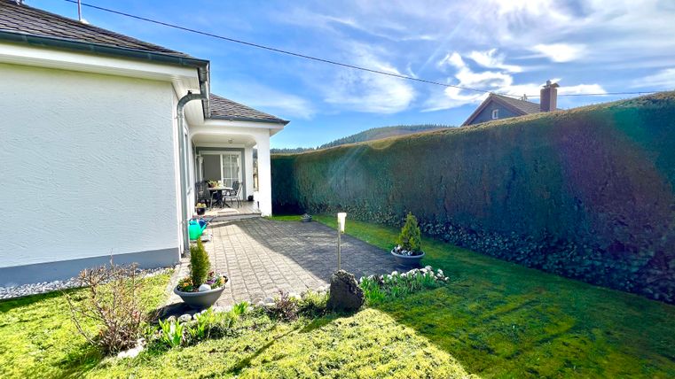 An inviting garden with green grass and a paved path. In the background, there is a bright house and a beautiful sky scene.