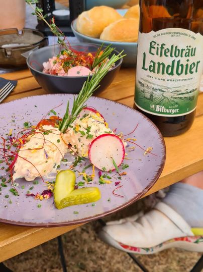 Ein schön angerichteter Teller mit Hähnchenbrust, frischen Kräutern und Radieschen. Dazu steht eine Flasche Eifelbräu Landbier und Brötchen auf dem Tisch.