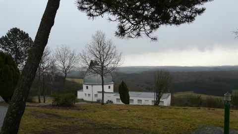 Eine malerische Kirche liegt in einer hügeligen Landschaft. Der Himmel ist bewölkt und die Bäume umgeben die Szenerie.