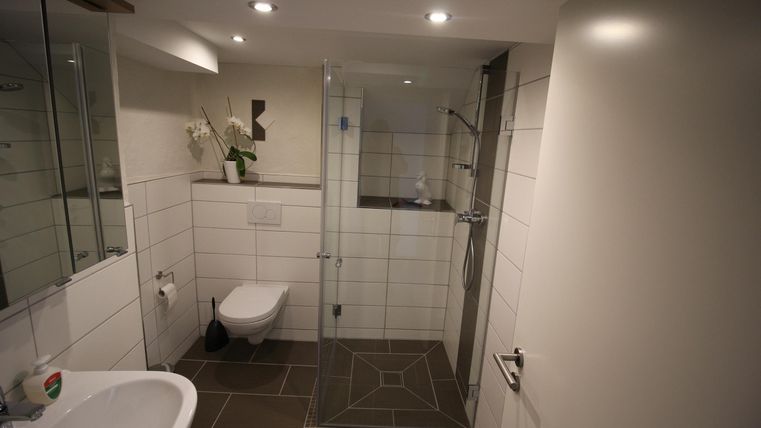 Een moderne badkamer met een inloopdouche en lichte tegels. De inrichting is eenvoudig en elegant.