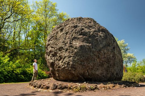 A large rock stands in a green environment. A person is looking at the rock in sunny weather.