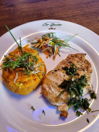 Een bord met gegrilde kipfilet, geserveerd met gepureerde zoete aardappelen en verse groenten. De gerechten zijn gegarneerd met kruiden en mooi opgediend.