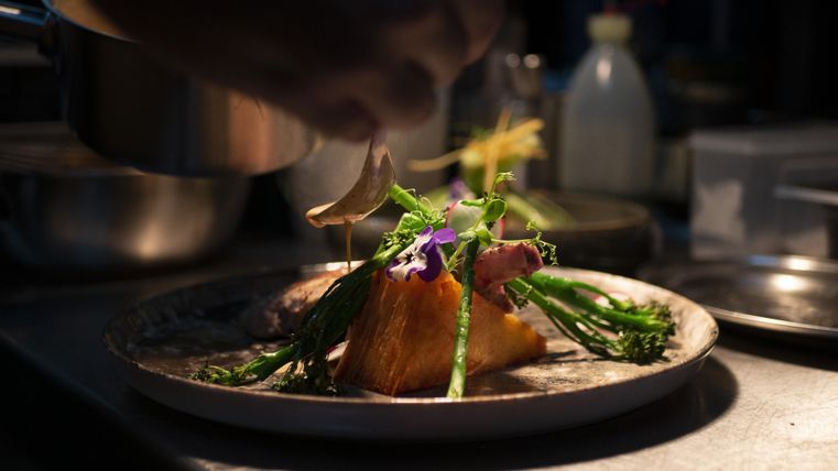Ein Teller mit liebevoll angerichtetem Essen wird zubereitet. Dazu gehören frisches Gemüse und essbare Blumen.