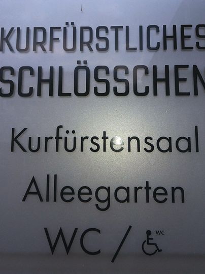 Een bord met de tekst "Kurfürstliches Schlösschen" en informatie over een evenementenruimte en een wc. Het bevat ook aanwijzingen voor de toegankelijkheid.