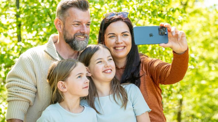 Een gezin maakt een selfie in de natuur. Ze glimlachen gelukkig naar de camera.