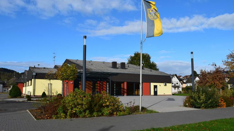 Een modern gebouw met een gele en zwarte façade. Op de voorgrond staan bomen en een vlaggenmast met een gele vlag.
