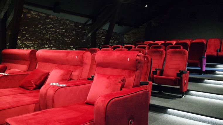 Ein modernes Kino mit roten, bequemen Sitzplätzen und einer stilvollen Atmosphäre. Die Beleuchtung sorgt für eine angenehme Stimmung.