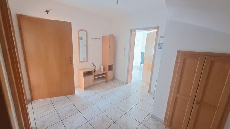 Ein heller Flur mit Fliesenboden und Holztüren. An der Wand befindet sich ein Spiegel sowie eine Garderobe.