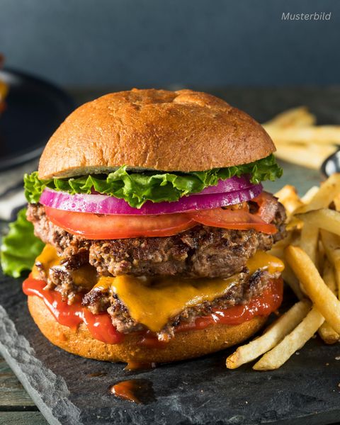 Ein saftiger Burger mit zwei Rindfleischpattys, Cheddar-Käse, frischem Salat, Tomaten und Zwiebeln. Dazu gibt es knusprige Pommes frites auf einem schwarzen Stein.