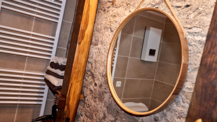 A modern bathroom with a round mirror and a stone wall.
Towels are neatly arranged and a radiator is visible.