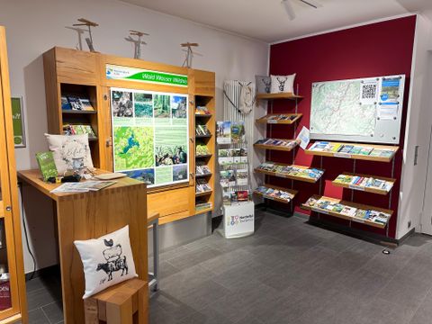 Een informatiecentrum met houten planken en brochures. Aan de muur hangt een kaart en er zijn uitnodigende zitplaatsen.