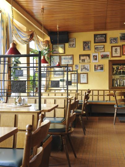 Ein gemütliches Restaurant mit Holztischen und Stühlen. An den Wänden hängen Fotos und die Wände sind in warmen Tönen gestrichen.