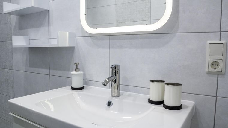 A modern bathroom with an elegant sink and a mirror. It includes decorative candles and bright tiles.