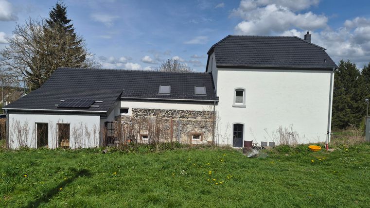 Ein modernes Haus mit einem flachen Dach und einer Steinfassade. Der Garten ist grün und von Wiesen umgeben.