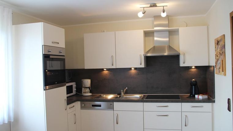 A modern kitchen with white cabinets and a dark countertop. It is well-equipped with a stove, microwave, and sink.