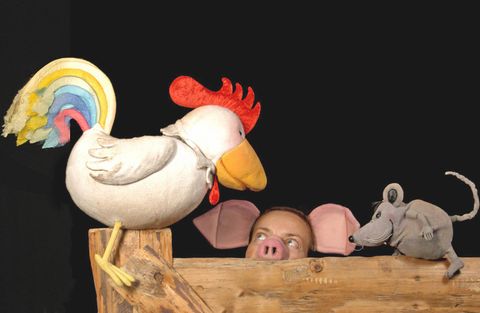 A colorful doll of a chicken with a rainbow on its back, on which a little mouse sits. In the background, the face of a person with a pig's head can be seen.