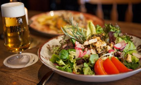 Ein frischer Salat mit gegrilltem Hähnchen, buntem Gemüse und Kräutern. Im Hintergrund steht ein Glas Bier.