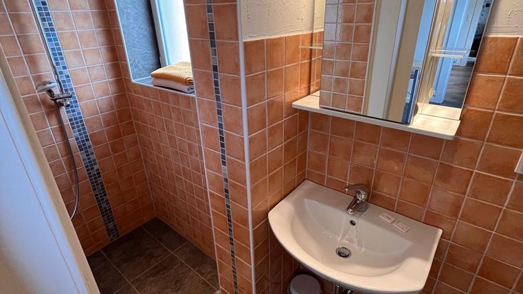 Ein modernes Badezimmer mit orangefarbenen Fliesen und einer Dusche. Es gibt ein Waschbecken und ein WC, sowie ein Fenster für Tageslicht.