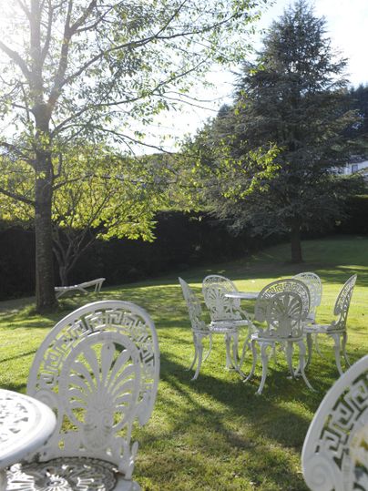 Ein schöner Garten mit weißen Gartenmöbeln auf grünem Rasen. Im Hintergrund stehen Bäume, und die Sonne scheint durch das Laub.