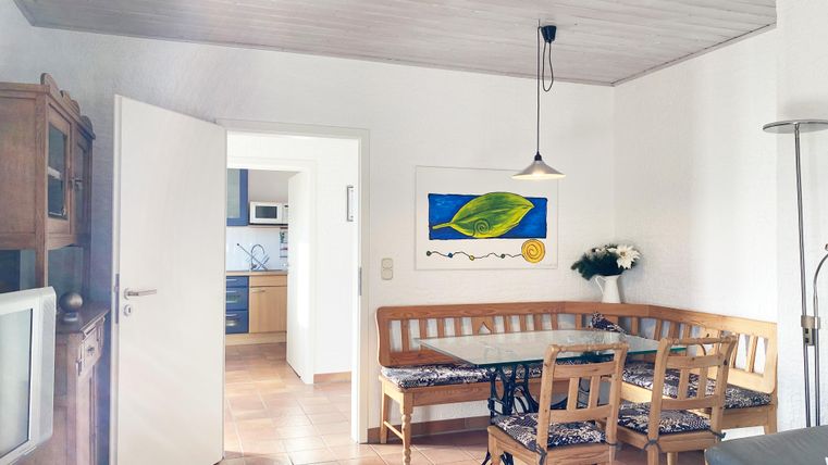 Ein helles Wohnzimmer mit einem Essbereich aus Holz und einem großen Tisch. Die Wände sind mit einem Kunstwerk und frischen Blumen dekoriert.