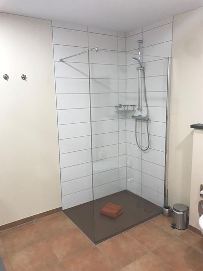 Eine moderne Duschkabine mit gläserner Trennwand und minimalistischer Ausstattung. Der Boden ist gefliest und ein Handtuch liegt auf dem Boden.