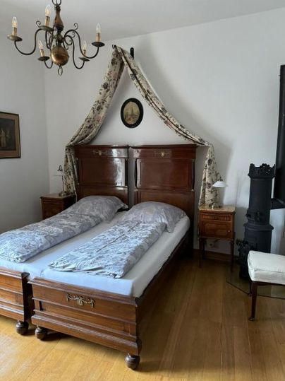 Een gezellige slaapkamer met een houten tweepersoonsbed en een elegante dekbed. De muren zijn eenvoudig, en een kroonluchter zorgt voor aangenaam licht.