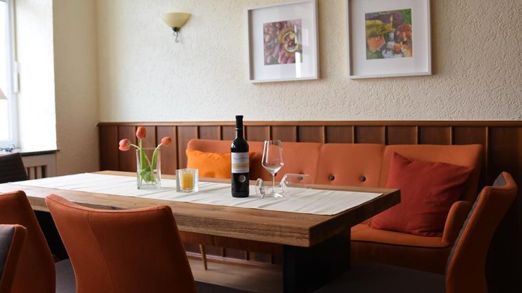 Ein gemütlicher Essbereich mit einem Holztisch und orangefarbenen Stühlen. Auf dem Tisch stehen eine Flasche Wein, Gläser und frische Blumen.