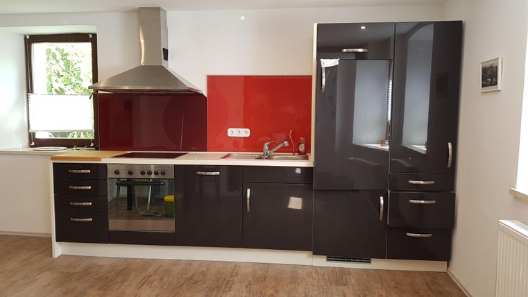 Moderne keuken met zwarte meubels en een rode achterwand. Goed verlicht en functioneel ingericht.