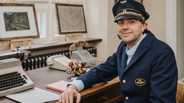 A man in a uniform is sitting at a desk. Next to him are a typewriter and various documents.