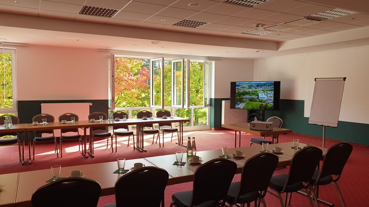 Een moderne vergaderruimte met tafels en stoelen. Grote ramen bieden uitzicht op de kleurrijke herfstbomen buiten.