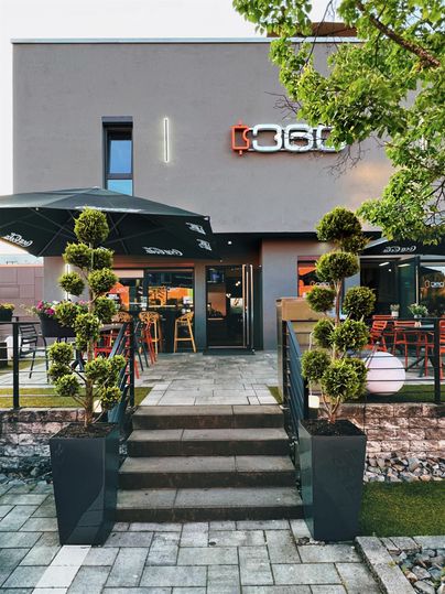 Een modern restaurant met een uitnodigende entree en elegante planten. Het terras biedt ruimte voor gasten om te ontspannen.