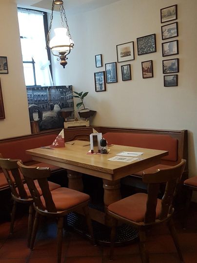 Ein gemütlicher Tisch mit Stühlen in einem Raum. An den Wänden hängen mehrere Bilder, und eine Lampe sorgt für warmes Licht.