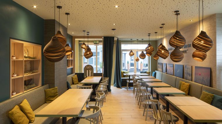 Een modern café met houtdecor en gezellige tafels. Zacht licht van hanglampen creëert een uitnodigende sfeer.
