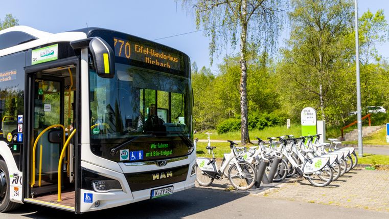 Ein moderner Bus der Linie 77 steht an einer Haltestelle. Daneben sind mehrere Fahrräder zum Ausleihen aufgestellt.