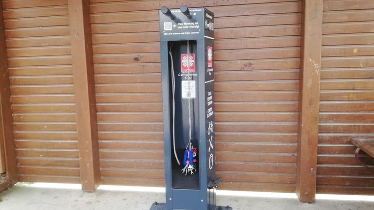 A washing station with a hose and a water tank is in front of a wooden wall. The station is intended for cleaning bicycles or equipment.
