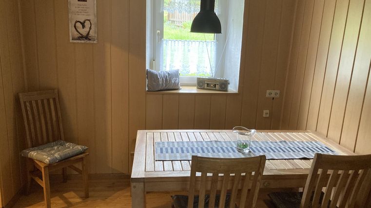 Een lichte eetkamer met een houten tafel en vier stoelen. De muren zijn van hout en een raam met uitzicht op buiten zorgt voor natuurlijk licht.