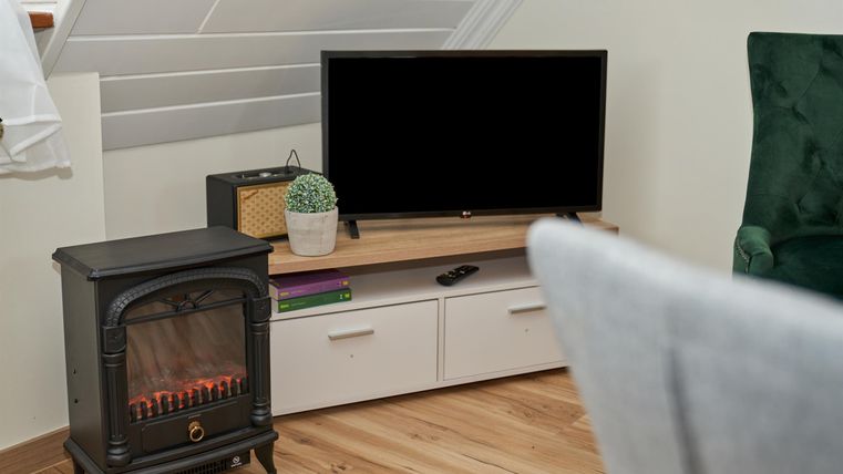 A cozy living room with a television and an elegant fireplace. The room has a modern style and a warm wooden floor.