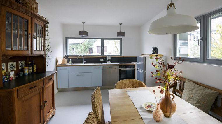 Eine moderne Küche mit einem Esstisch und Stühlen. Helle Wände und große Fenster sorgen für eine freundliche Atmosphäre.