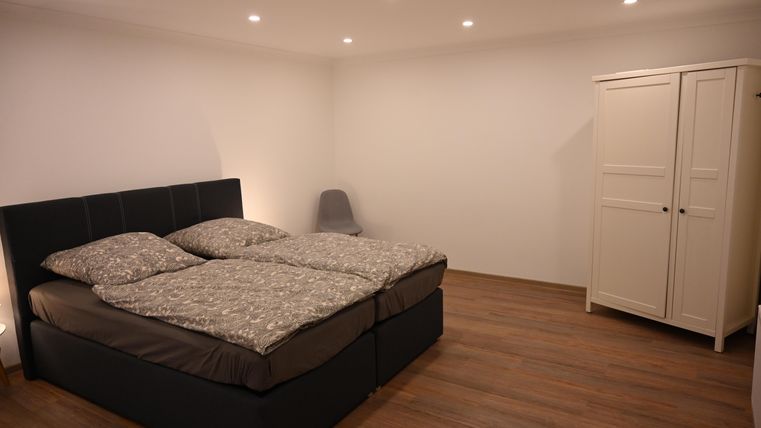 Een moderne slaapkamer met een tweepersoonsbed en een comfortabele zithoek. De ruimte heeft lichte muren en een mooie houten vloer.